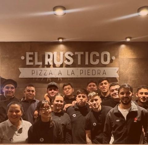 El equipo de El Rústico posando en el salón, bajo el cartel Pizza a la piedra
