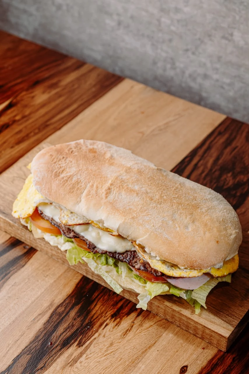 Lomito completo de 28 cm con carne, huevo, jamón, queso, lechuga y tomate sobre una tabla de madera